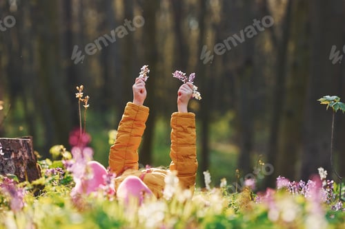 Preview: Happy little girl in casual clothes lying down on ground in spring forest at daytime