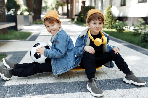 Preview: Two stylish twin boys sitting on the skateboard or pennyboard looking each over up in the street.