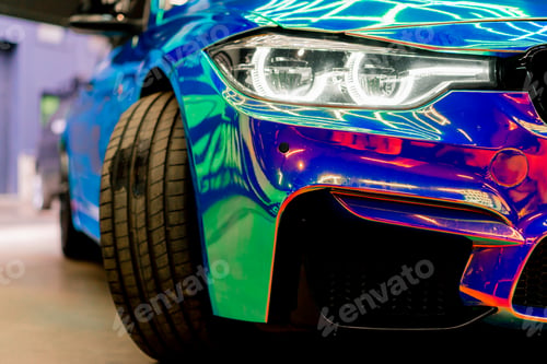 Preview: Close-up of headlight wheel and bumper of luxury car covered with protective film in chameleon color