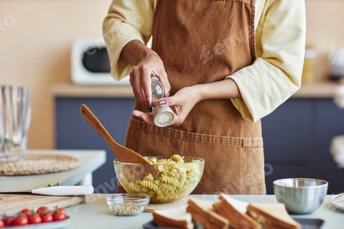 Preview: Black woman adding spices to pasta cooking in kitchen