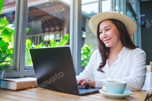 Preview: Portrait image of a young woman with hat working on laptop computer in cafe