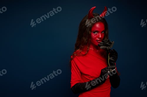 Preview: A stunning woman dressed in a vibrant red outfit with devil horns, holding a black rose elegantly
