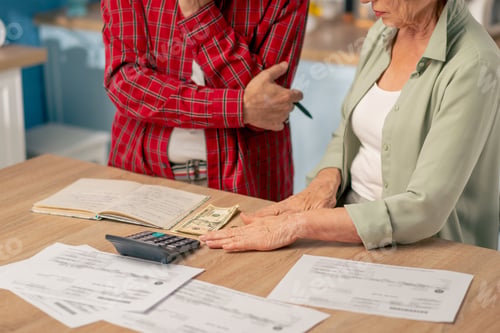 Preview: in bright kitchen an elderly couple at the table count their expenses monthly payment summing up the
