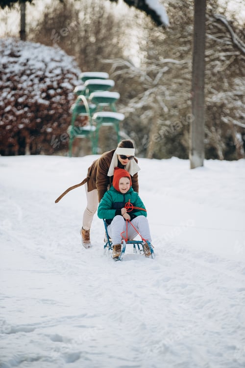 Preview: Mother pushing son on sled in winter park
