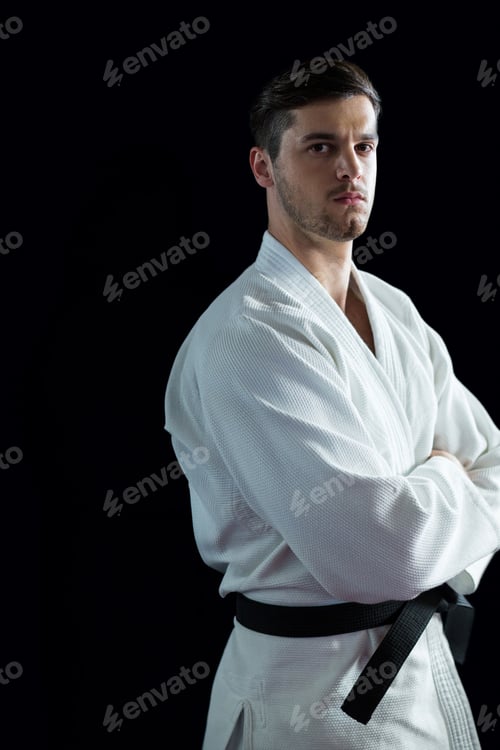 Preview: Male martial artist wearing white gi, black belt in studio against black backdrop looking serious