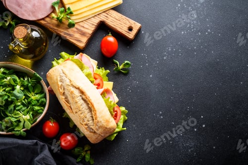 Preview: Ciabatta sandwich with lettuce, cheese, tomatoes and ham on black table.