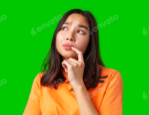 Preview: Young woman in bright orange shirt on green background appears thoughtful while pondering a question