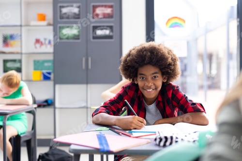 Preview: Portrait of happy african american schoolboy writing at desk, with diverse pupils, copy space