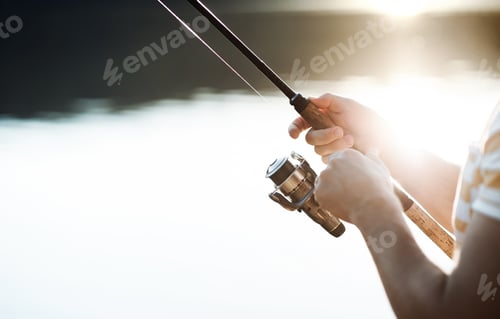 Preview: Midsection of a man fishing by a lake, holding a rod. A close-up.