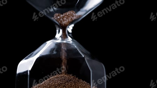 Preview: Close up of flowing sands in sandglass on a black background.