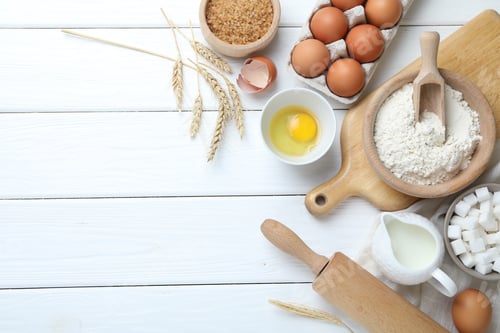 Preview: Rolling pin and ingredients for dough on white wooden table, flat lay. Space for text