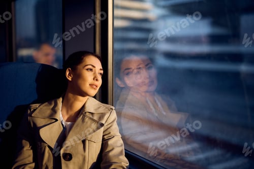 Preview: Young woman day dreaming by the window while riding in a train at sunset.