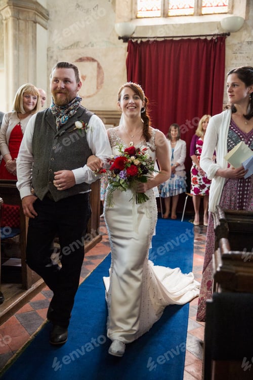 Preview: Smiling bride and groom walking down the isle in a church.