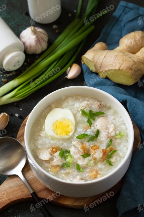 Preview: Arroz Caldo Soup. Hot soup with ginger chicken rice and garlic in a bowl on a dark countertop.