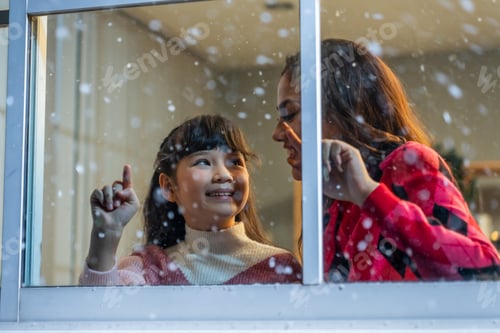 Preview: Adorable child looking at the window and admire snowflakes with mother.
