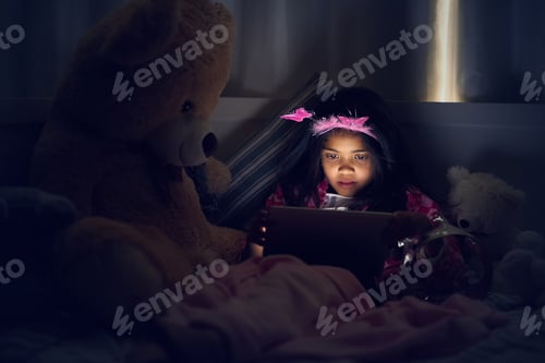 Preview: Cropped shot of a little girl using a digital tablet while lying in bed with her teddy at night