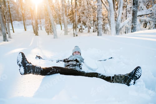 Preview: Young man having fun in snow outdoors in winter, lying in snow.