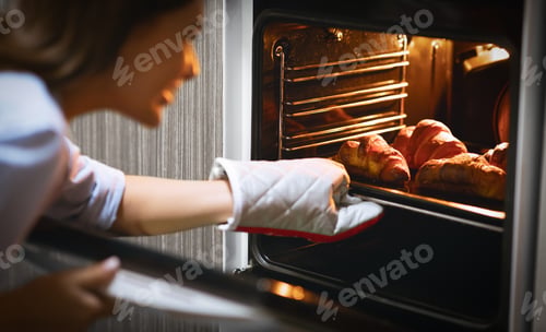 Preview: Happy woman removing hot croissants from oven at home