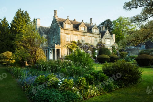 Preview: Exterior view of a 17th century country house from a garden with flower beds, shrubs and trees.
