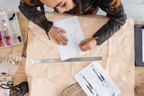 Preview: Top view of african american craftswoman drawing sketch on sewing print in workshop