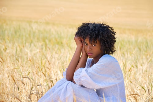 Preview: african american girl in white dress sitting in a wheat field looking at camera
