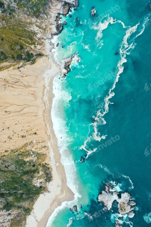 Preview: Vertical overhead shot of the beautiful shoreline of the sea with blue clean water and sandy beach