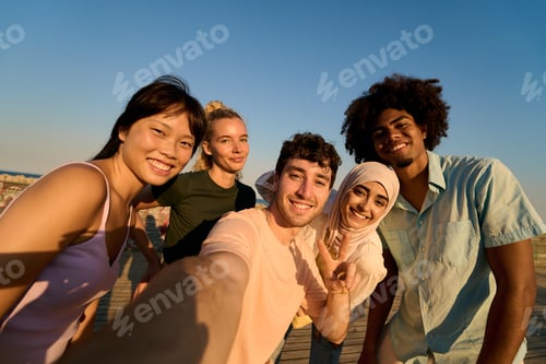 Preview: Happy multi ethnic friends taking selfie at sunset on pier