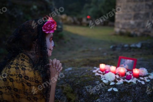 Preview: Woman celebrating day of the dead praying at grave with candles and flowers