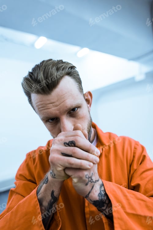 Preview: tattooed prisoner covering mouth with hands and looking at camera