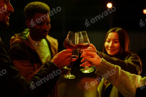 Preview: Friends enjoying a lively celebration outdoors while clinking glasses in the evening