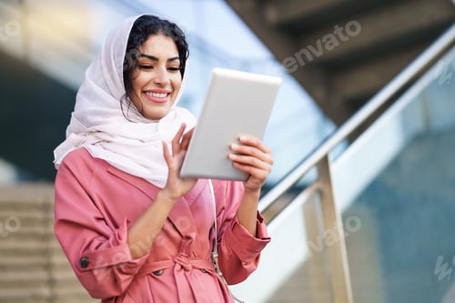 Preview: Young Arab woman wearing hijab using digital tablet outdoors