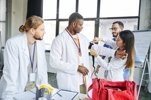 Preview: asian woman in white coat applying compressive tourniquet on arm of african american student near
