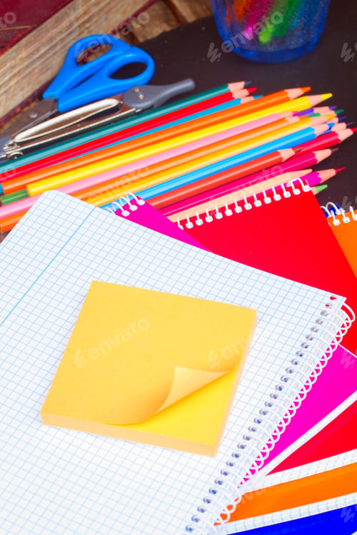 Preview: Empty notebook and set of colorful pencils on black board