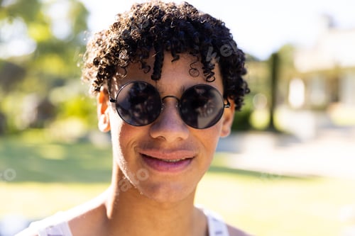 Vista previa: Close-up portrait of handsome biracial young man wearing sunglasses and posing in yard