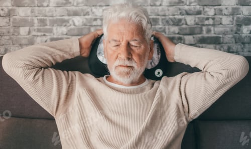 Preview: Handsome senior man sitting on the couch with a massage pillow behind his head, closed eyes