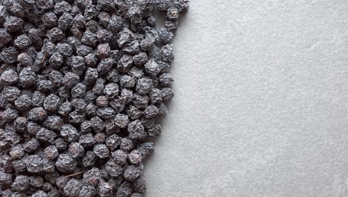Preview: Close up photo of organic dried aronia berries on a dark slate background, selective focus.