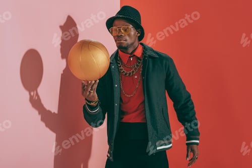Preview: stylish african american man in hat and sunglasses holding golden basketball ball