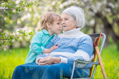 Preview: Little boy telling a secret to his great grandmother in a blossoming orchard