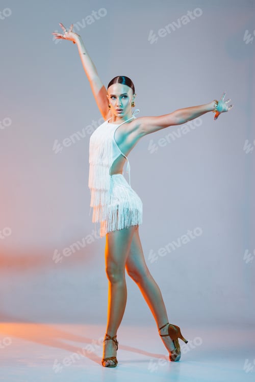Preview: Elegant dancer strikes a bold pose in a white fringe outfit with dramatic lighting in studio.