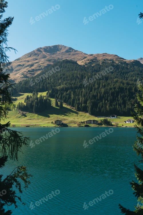 Preview: Alpine lake reflecting mountains, forest, green shore buildings davos
