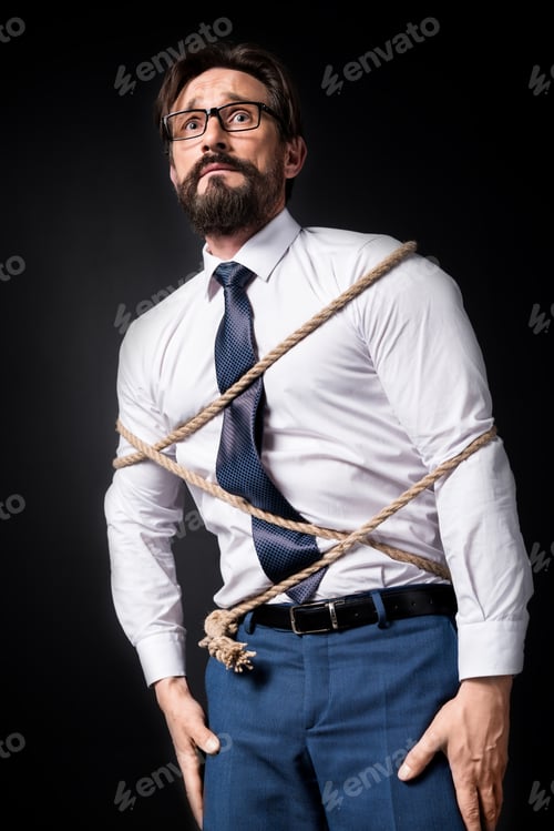 Preview: scared middle aged businessman in eyeglasses standing tied with rope isolated on black