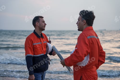 Preview: Engineers discussing with colleague by the sea at sunset