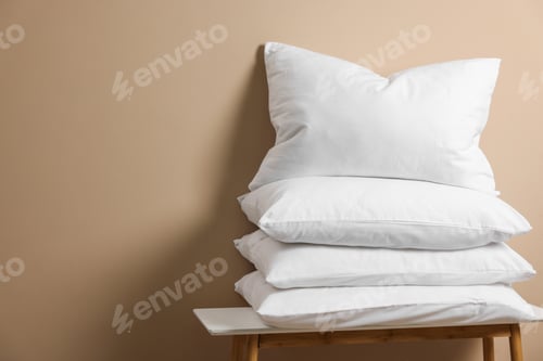 Preview: Stack of soft white pillows on table near beige wall. Space for text