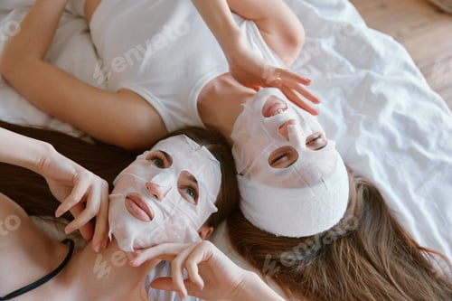 Preview: Two young cheerful woman applying facial mask overhead view