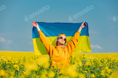 Preview: Woman in yellow hoodie and ukrainian flag in rapeseed field