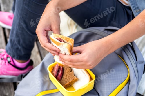 Preview: Close-up of hands holding sandwich on background of lunchbox and school backpack