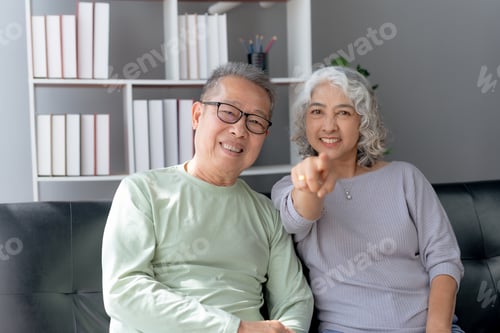 Preview: Happy elderly Asian couple laughing bonding together sitting sofa at home.