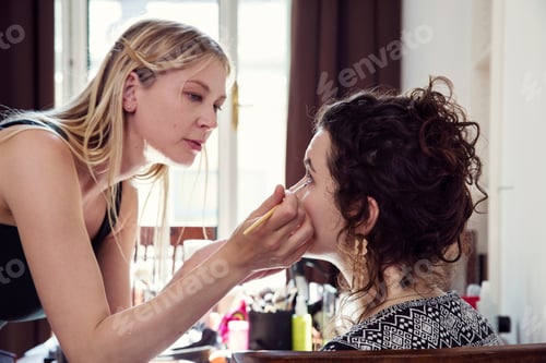 Preview: Woman applying friend's eye liner in bedroom