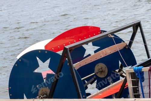 Preview: Close-up of a colorful paddle wheel on a boat docked by the water on a sunny day.
