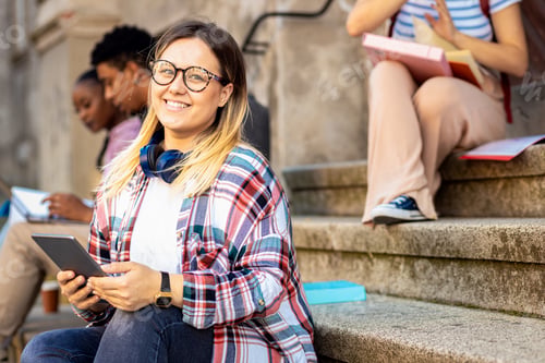 Preview: Female student sits on the stairs and using tablet.